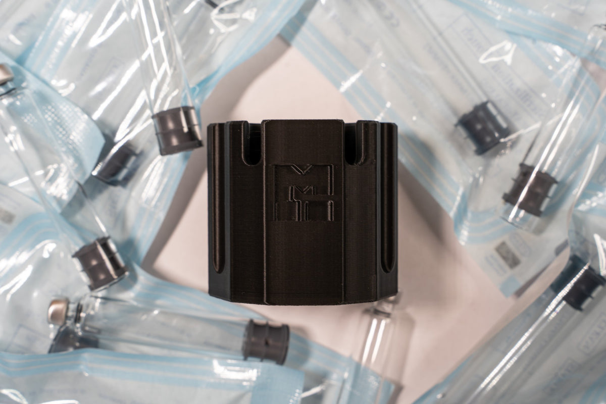 MODTECH purge station from the front, showing the M logo, surrounded by 3 mL cartridges sealed in their sterilization pouches
